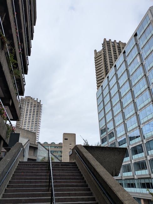 A high-rise residential building with multiple balconies and a vertical window pattern seen from the ground level, part of a concrete urban block during daytime. The building's exterior features textu